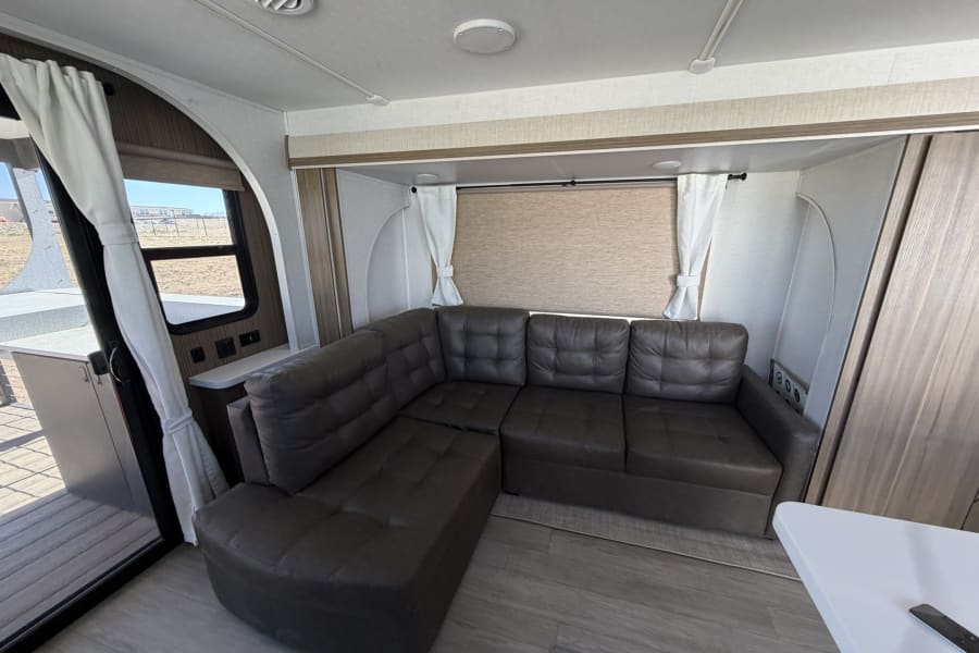 Spacious RV rental interior: a bright living area featuring a comfortable L-shaped sofa, windows, and light decor.