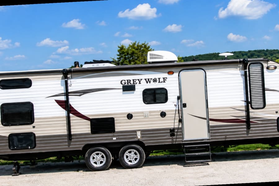 Grey Wolf travel trailer rv rental under blue sky. Parked on gravel, ready for camping trips and outdoor adventures.
