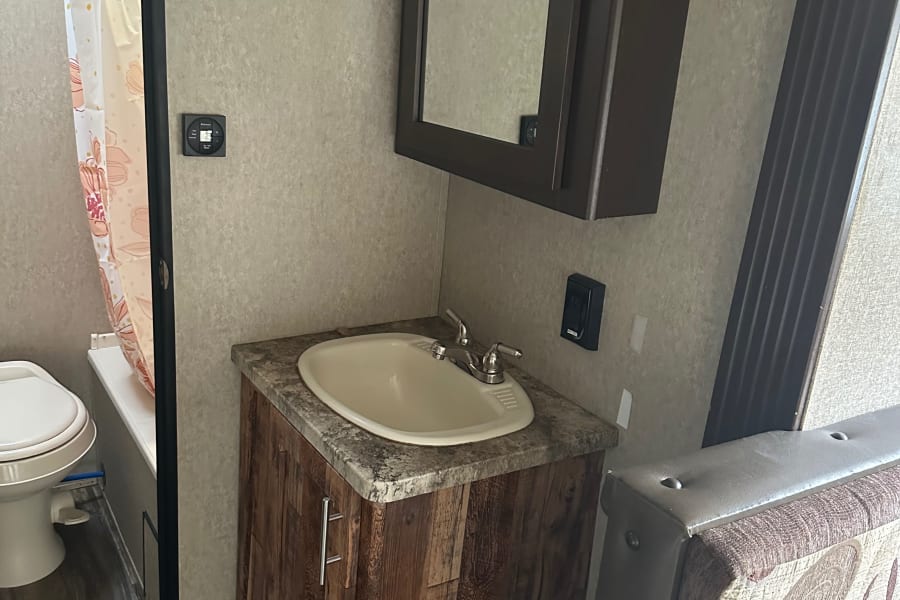Clean RV rental bathroom features a sink vanity, toilet, shower, and modern controls, perfect for your journey.