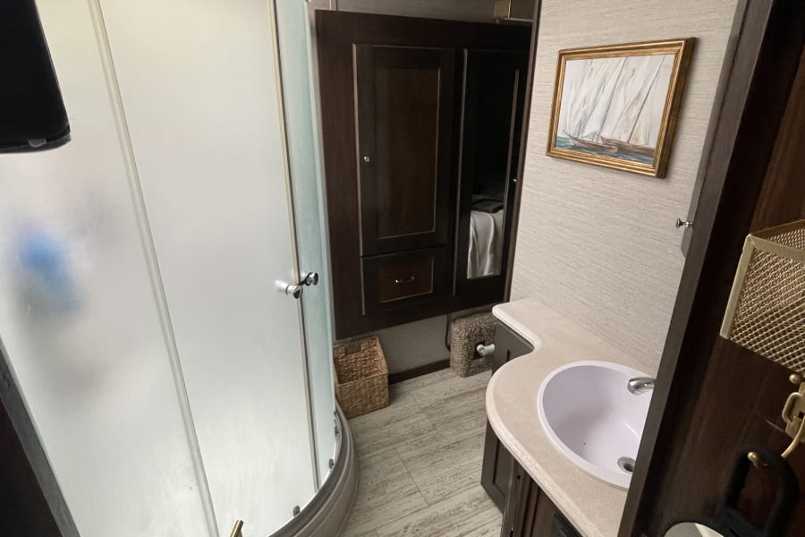 This RV rental bathroom features a compact shower, toilet, and vanity with sink. Enjoy a skylight and modern finishes.