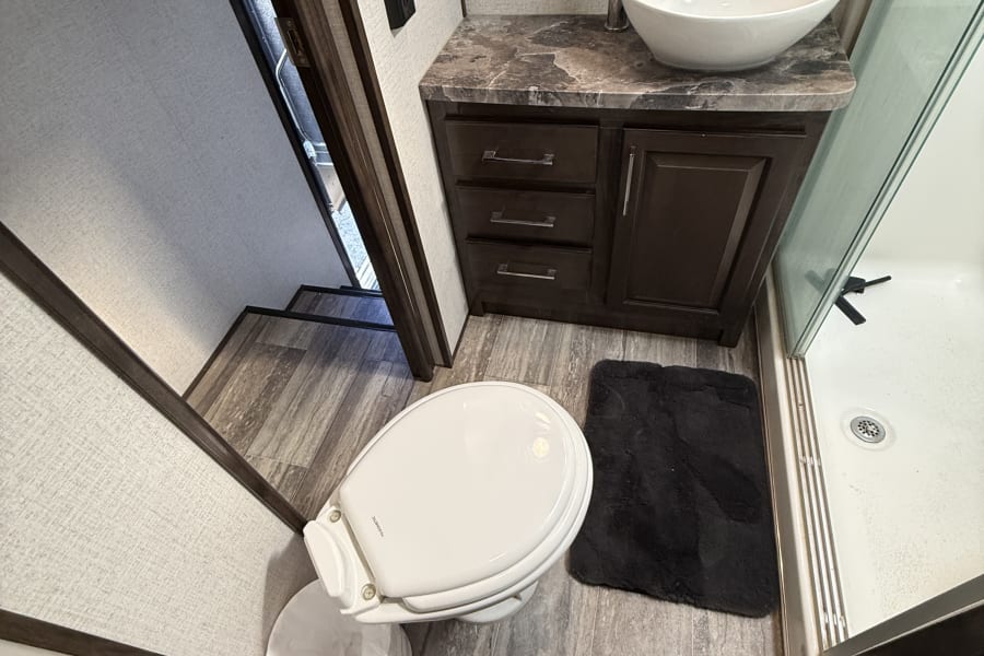 Inside an **rv rental**: a compact bathroom with a white toilet, sleek vessel sink on a dark vanity, and a shower with glass doors.