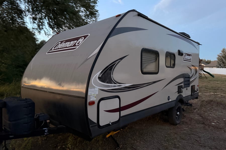 Explore the outdoors with this Coleman travel trailer, ideal for an RV rental, shown parked at dusk.