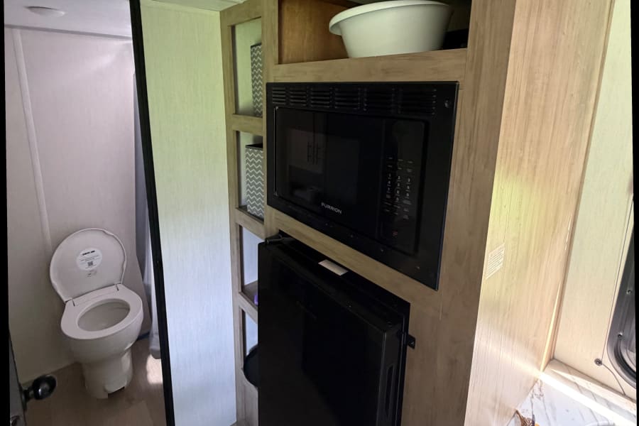 RV rental interior features a compact toilet on the left, and a kitchen unit with a microwave and fridge on the right.