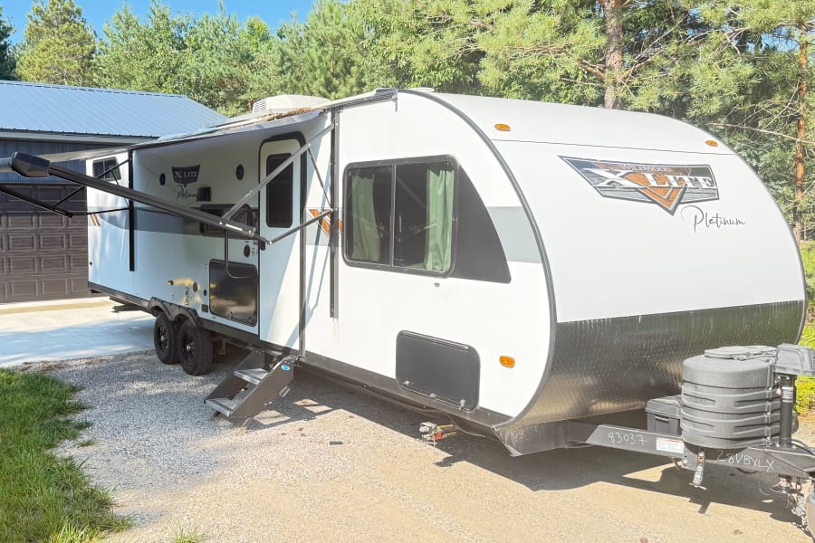 A white Wildwood X Lite Platinum travel trailer, featuring an extended awning, parked outside for your rv rental.