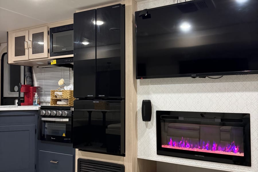 This modern rv rental features a compact kitchen, Furrion fridge, Summit TV, and a cozy Greystone electric fireplace.