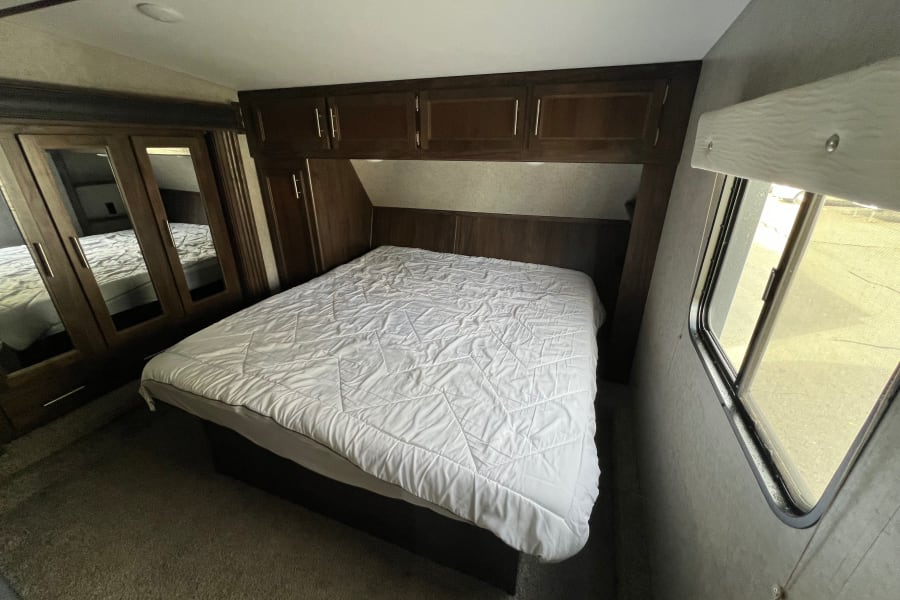 RV rental interior: A cozy bedroom with a queen bed, white comforter, mirrored wardrobe, and overhead cabinets.