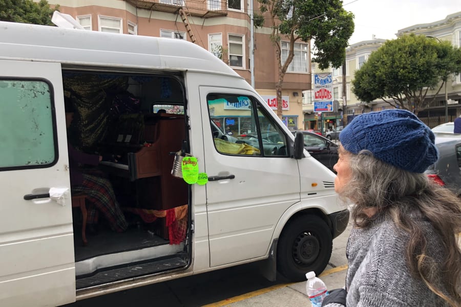 A street performer plays piano inside a converted van, resembling an RV rental, captivating a woman spectator.