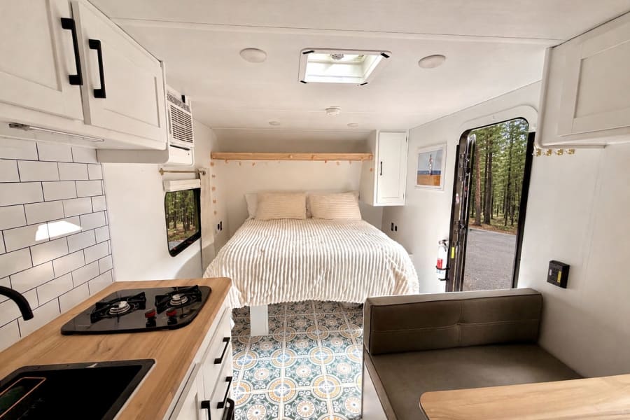 Cozy, modern RV rental interior featuring a full kitchen, comfy bed, dinette, and bright, patterned flooring.