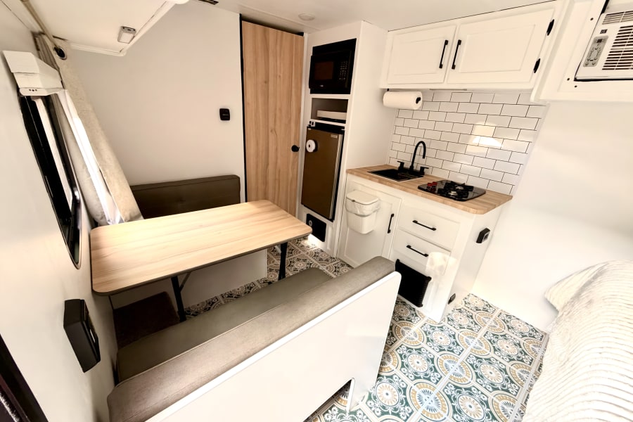 Bright rv rental interior with a cozy dining booth, sleek kitchen with white cabinets, and a vibrant patterned floor.