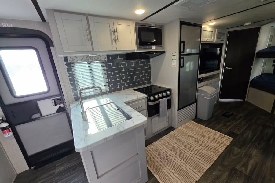 Spacious RV rental kitchen with modern light cabinets, dark floors, and full amenities, perfect for road trips.