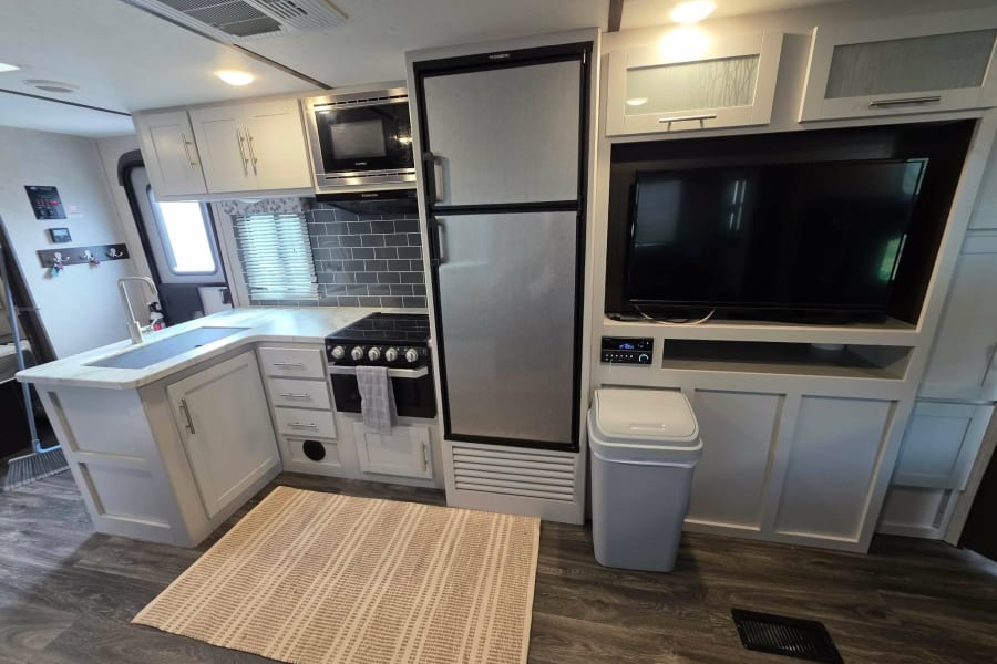 Modern RV rental kitchen & living area features a full fridge, microwave, and TV. Bright, clean interior for comfortable travel.
