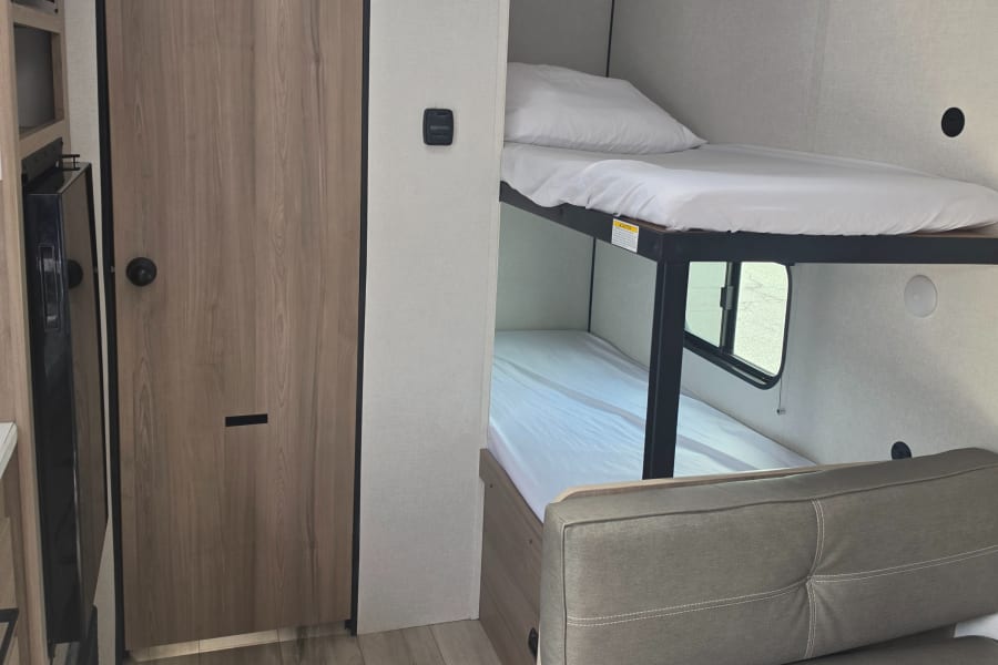 Modern rv rental interior with stacked bunk beds, a cozy sofa, and cabinet storage, ideal for family travel.