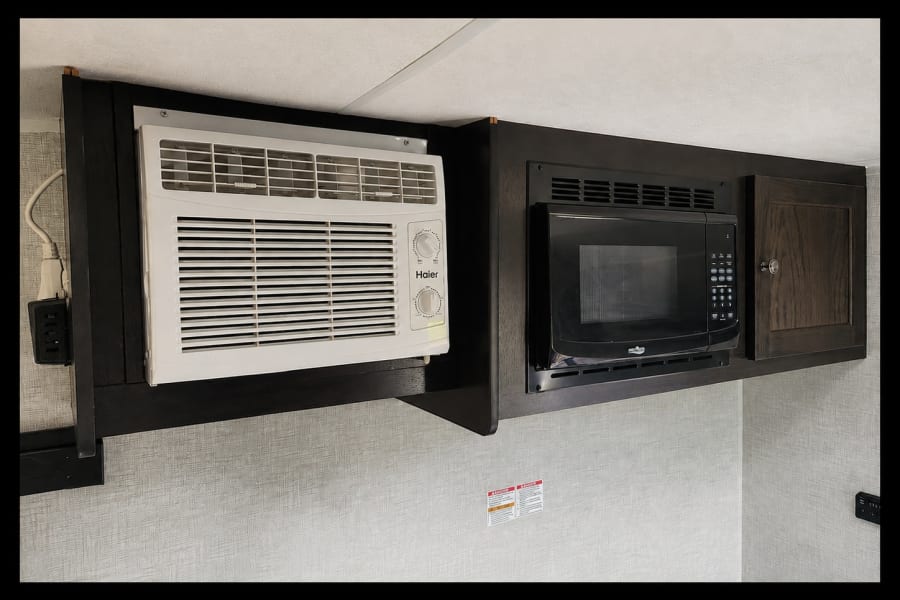 RV rental: Overhead cabinets hold a compact AC unit and built-in microwave, efficiently furnishing a small living space.