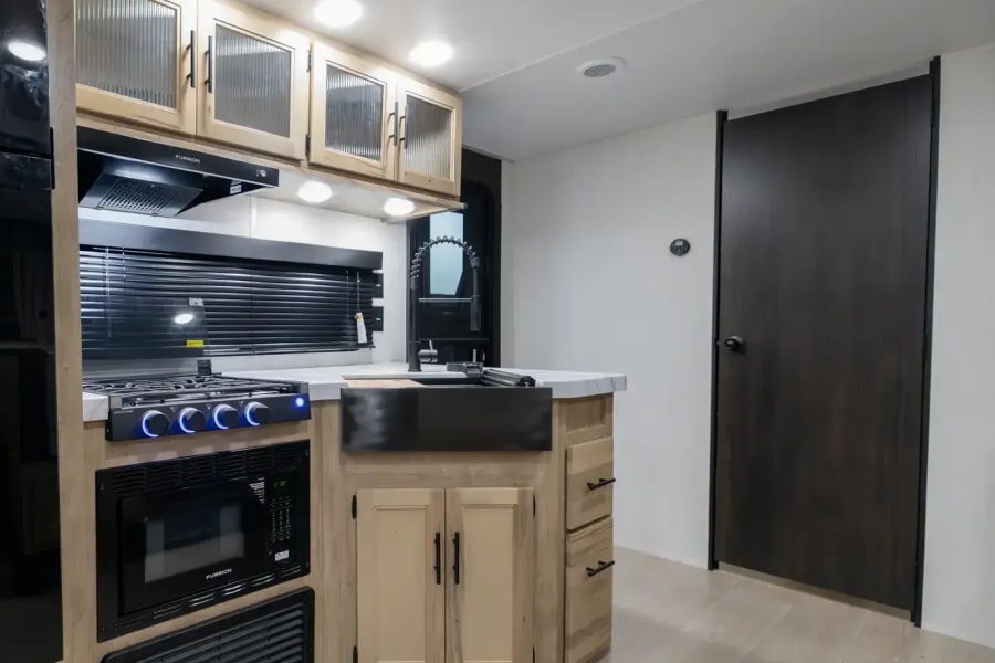 Modern RV rental kitchen with light wood cabinets, black appliances, and a farmhouse sink, perfect for road trip cooking.