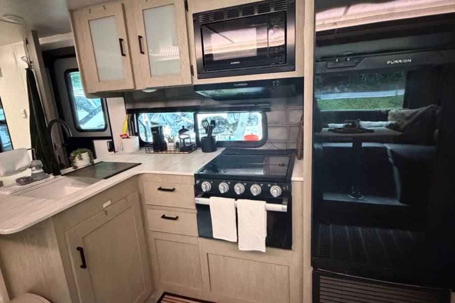 Clean RV rental kitchen with microwave, stovetop, sink, and large fridge. Ready for your next adventure!