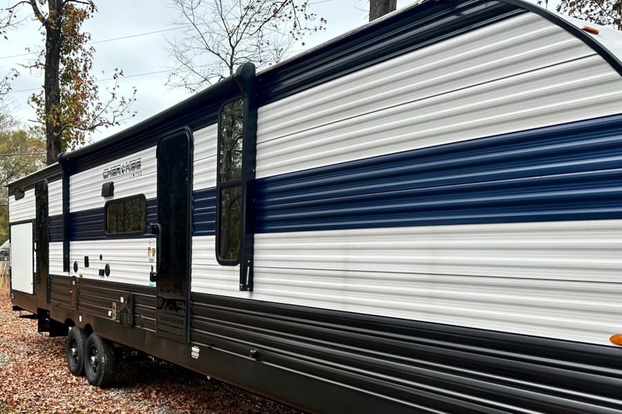 A young child plays among autumn leaves next to a white and blue Cherokee Limited RV rental, showcasing a serene outdoor camping scene.