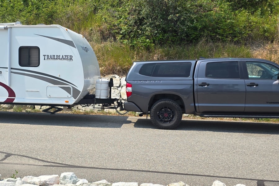 A grey pickup truck towing a white Trailblazer travel trailer. This RV rental is ready for your next camping adventure.