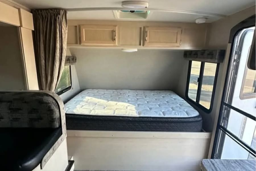 This rv rental offers a bright, compact interior with a comfy bed, overhead cabinets, and a partial view of dinette seating.