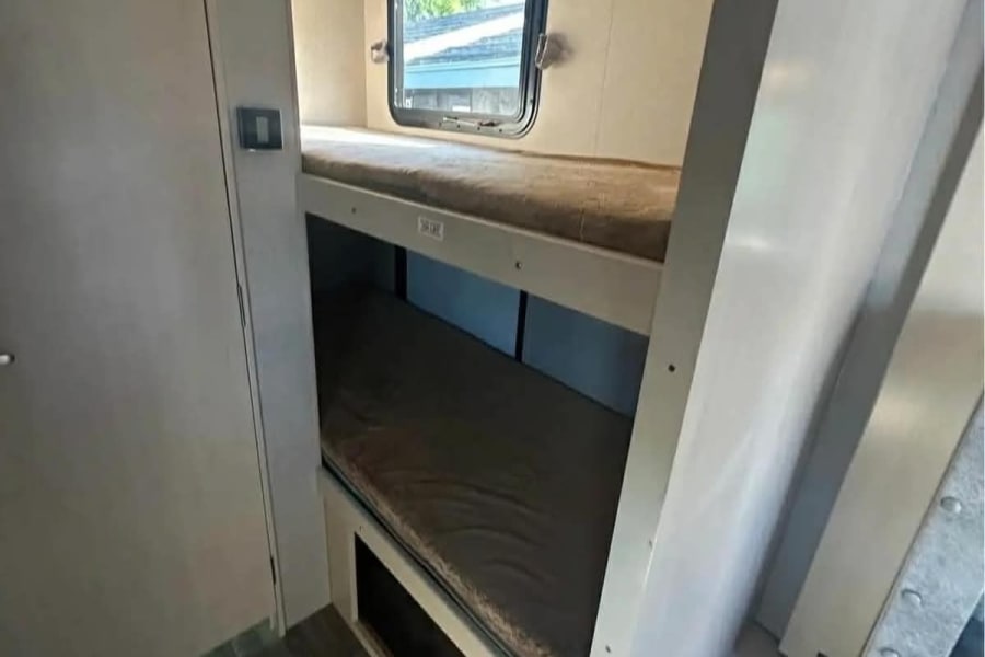 Inside an rv rental, functional bunk beds with mattresses and a window offer compact sleeping for travel.