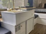 An rv rental interior featuring a compact kitchen with a sink/stove, a cozy bed, and an AC unit for adventures.