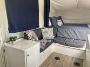 Modern RV rental interior: bed, gray lounge, and marble counter in a cozy pop-up camper.