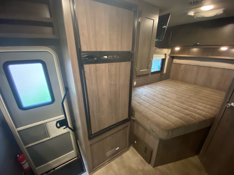 Wide shot of back of coach showing exterior door, refrigerator with separate freezer and queen bed. 