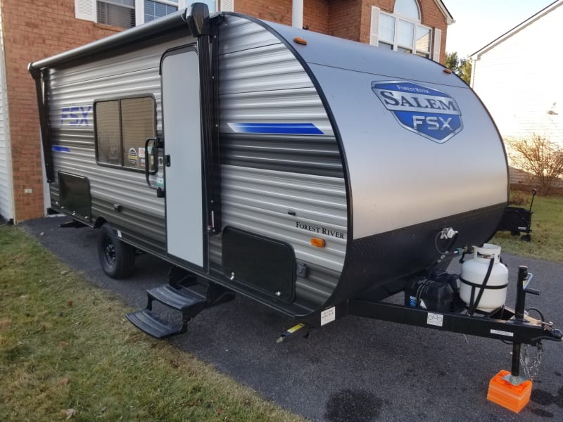 Flush passenger side view of the camper, tow approved. Offers large dinette window, retractable stairs, two under cabin storages and propane tank.