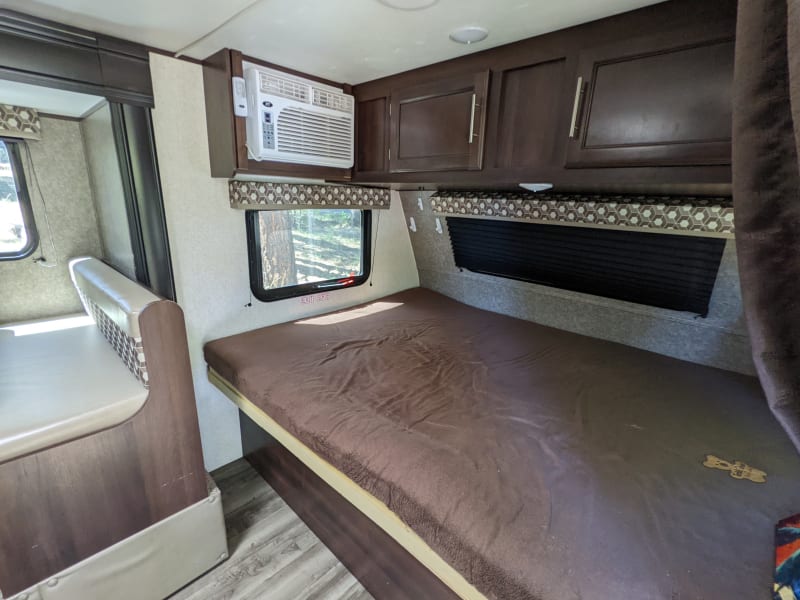 Queen size bed at front of trailer with privacy curtain.  Storage and AC unit above the bed.  