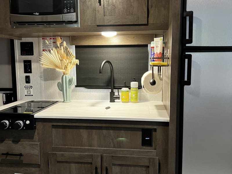 Kitchen with stove, microwave, fridge, toaster, kerig, water kettle, plastic plates and cups, coffee mugs, utensils. 