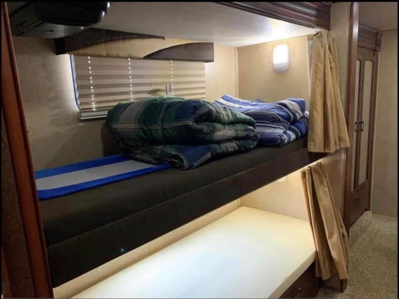Shown here with a not-included foam mattress topper, the bunks each have their own TVs with Boss wireless headphones and privacy curtains.