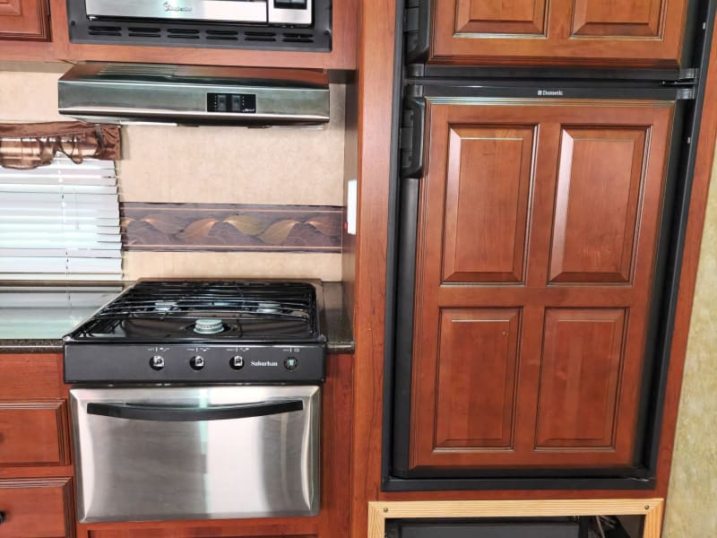 Propane stove and oven with vent hood, microwave, and fridge/freezer.