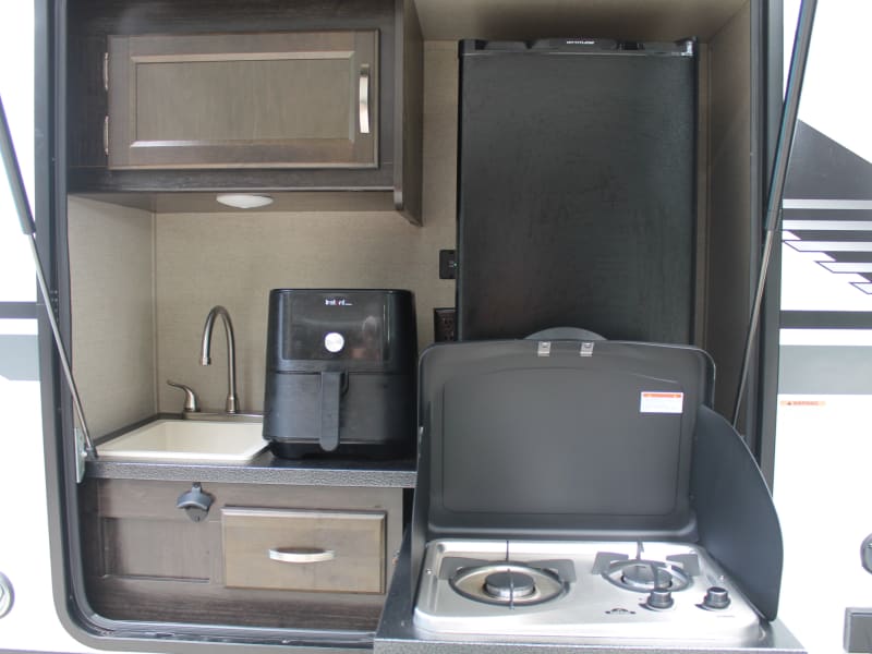 Outdoor kitchen has a sink, fridge, two burner cooktop, and air fryer