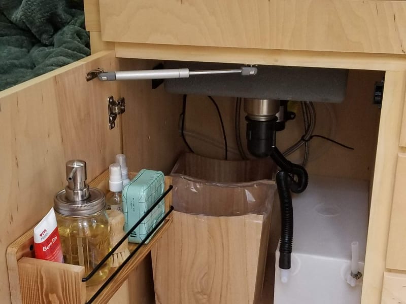 Under the kitchen sink there is a 3 gallon grey water storage that is easy to remove and empty, dish/hand soap, dish scrubber and a first aid kit.