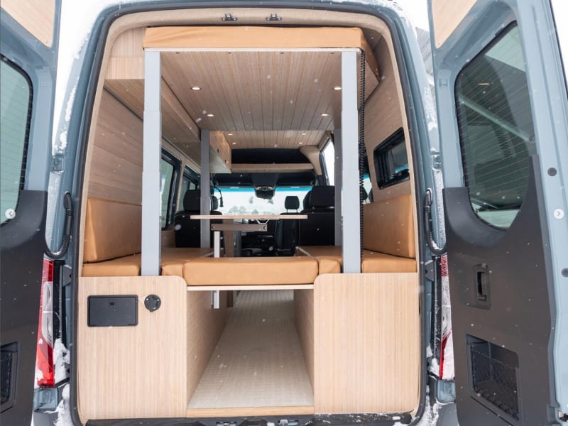 The dinette lounge can easily and comfortably seat 5 for a meal or board game. When it's time for bed, a simple button push lowers the top bed into position. The hookups for the outdoor shower and water tank fill port can also be seen in this photo at the rear of the left bench.