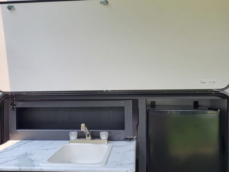 Pull-out camp kitchen with utensil drawer, sink, spice rack, and mini fridge.