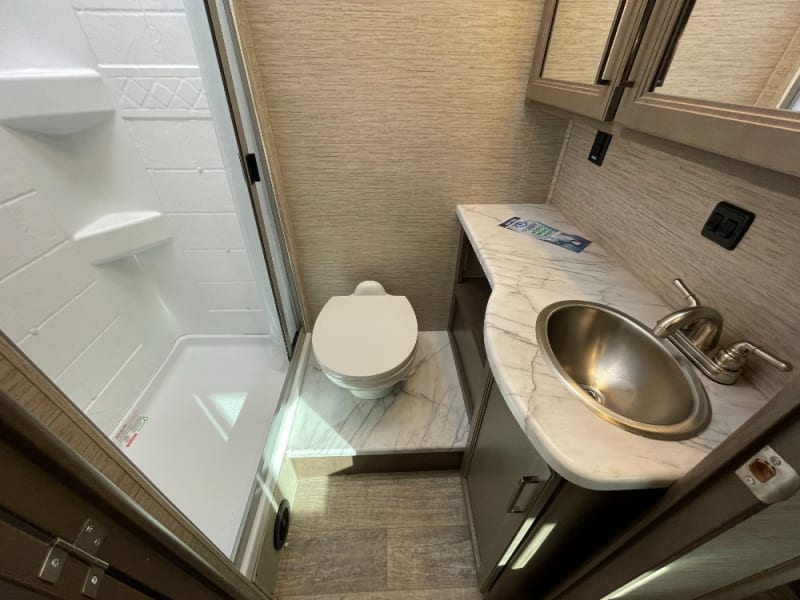 Private bathroom with toilet, shower and a sink with cabinets on top and bottom.