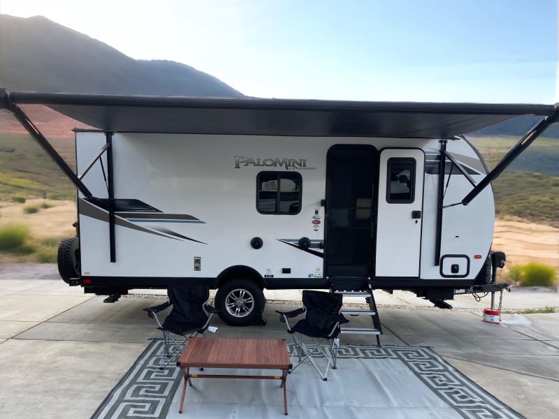 Main entrance of trailer with 15 foot power awning extended, area rug, table, and two camping chairs. Contact your host if you need additional chairs.