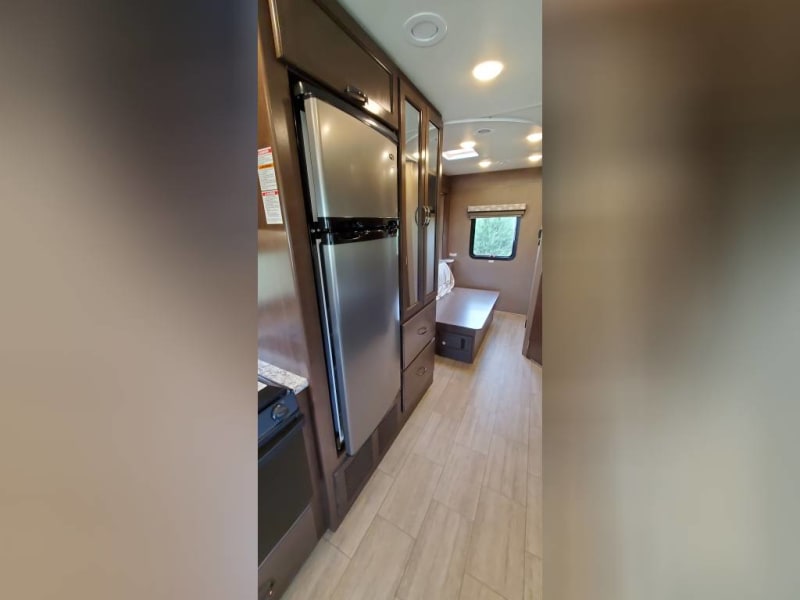 Refrigerator next to the stove, mirrored storage for hanging and drawers below. 