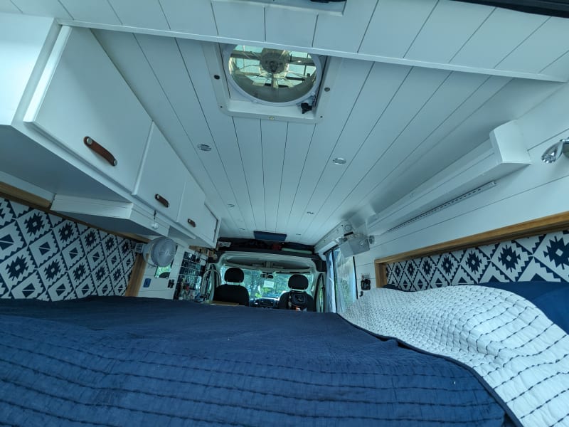 View of bedroom thru rear doors, showing overhead cabinets, headboard shelf, overhead and bedside reading lights, ceiling and wall mounted fans