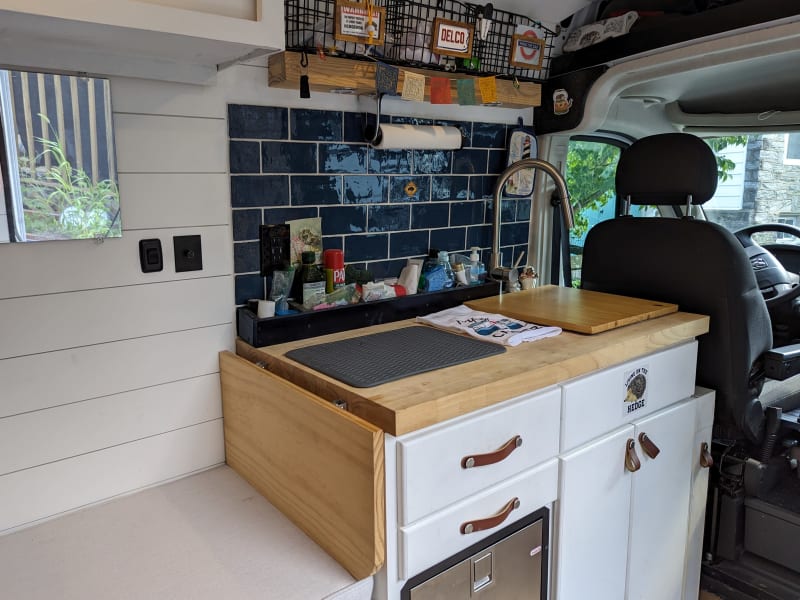 Kitchen sink with cutting board cover; stainless fridge; drawers/cabinet; butcher-block counter/extension leaf; wire baskets; slide-out storage unit