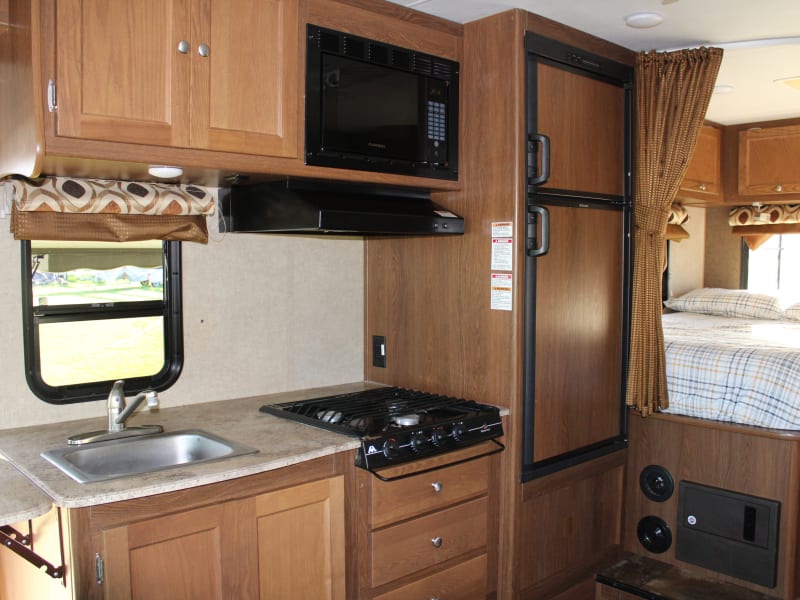 Kitchen area with counter end pop up counter extender.  Three burner propane stove, Microwave oven, medium size refrigerator / Freezer - Propane/Electric. 