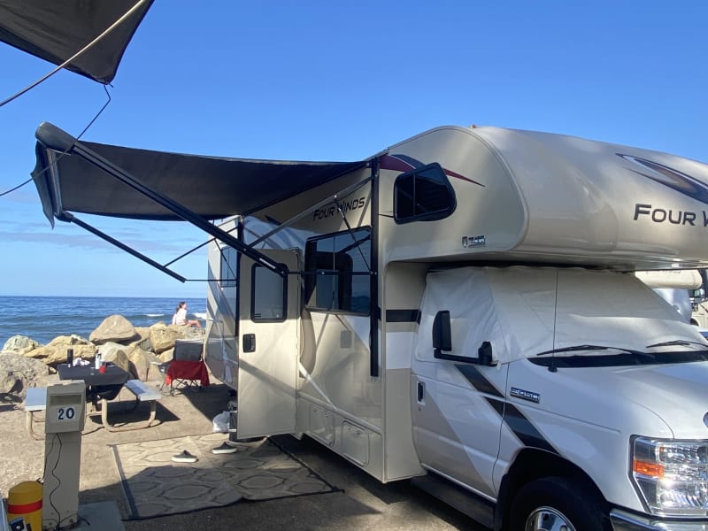 Relaxing in the shade at Faria Beach with the awning out! 🌞🚐 But remember—always use caution when setting up your awning. Strong winds and unexpected weather can cause damage, so secure it properly and retract when needed!