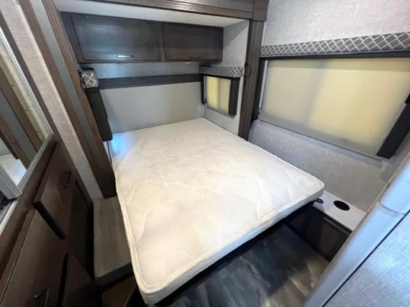 View of primary bed without the foam mattress topper or luxury linens. Storage cabinets above and below bed.