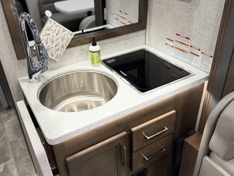 View of kitchen area with sink cover removed, cover down over stop top burner. 