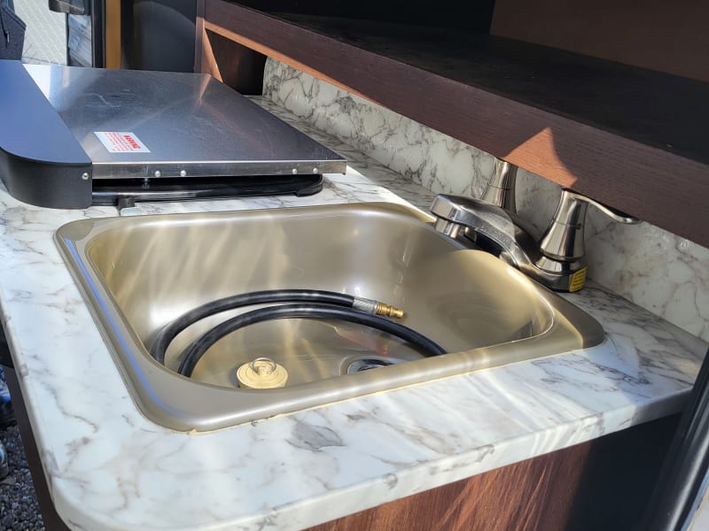 Exterior of trailer features stove top, sink and faucet and small refrigerator for outside enjoyment.
