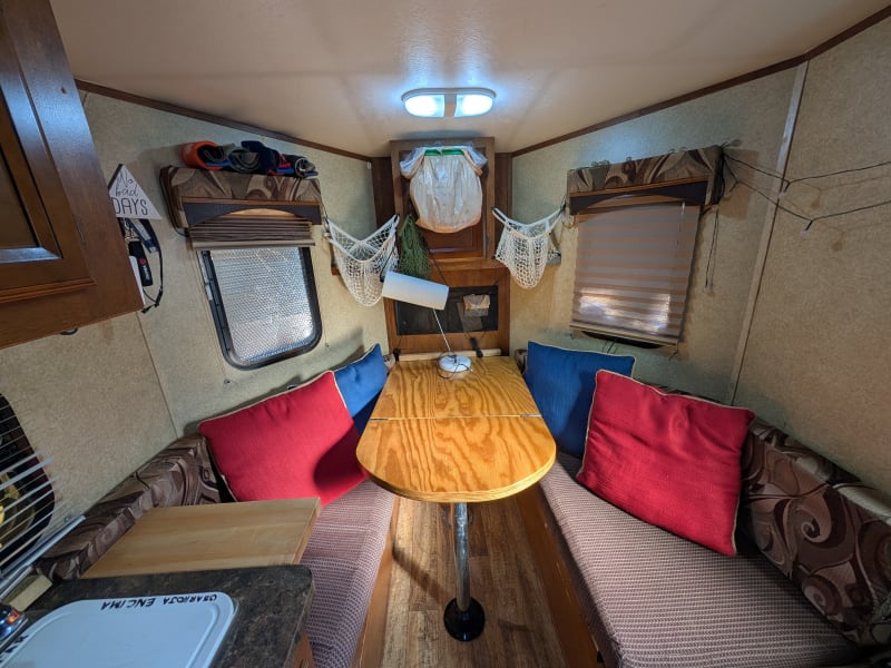 Convertible dinette. Table can be split to use the square piece as an outdoor table and shift the rounded piece against the wall. Also visible is the fold-up butcher block counter extension, which can - of course - also be dropped for ease of entry on the left side. In the cupboard in the center are the pots and pans (visible in photo below). Above it, we use a plastic bag for recycling; shelves each sides, and white & green nets we use for produce. Blue and red pillows can be used outdoors.