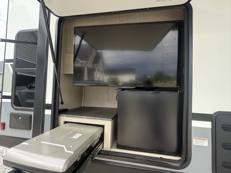 Enjoy the outdoor kitchen featuring a mini fridge, TV, and a convenient pull-out Coleman grill — perfect for cooking and relaxing outside.