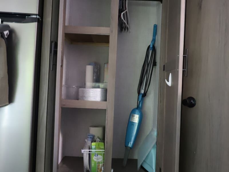 Pantry closet is designed for both storage and convenience. One side is designated for food and dry goods, including provided paper products supplied by the host for easy use during your stay. The opposite side offers a practical space for hanging clothes to keep them neat and organized, along with storage for a vacuum and broom to help maintain cleanliness throughout the camper.