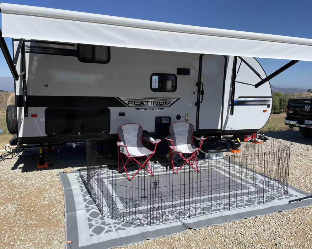 Outdoor living area with awning, outdoor rug, chairs, griddle, refrigerator, &amp; LED lights.