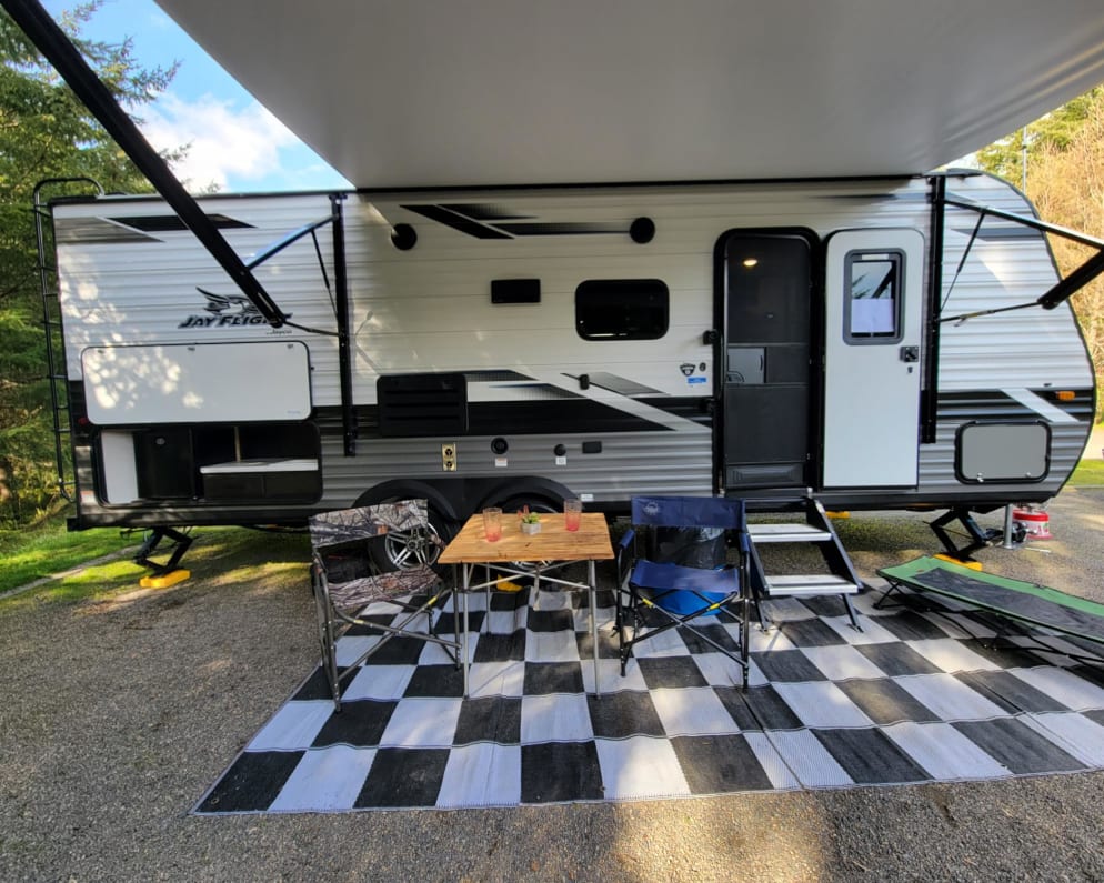 Outdoor mat provided with camp chairs and wood top collapsible table.